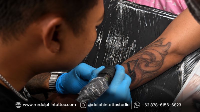 Tattoo artist wearing blue gloves working on a detailed forearm tattoo